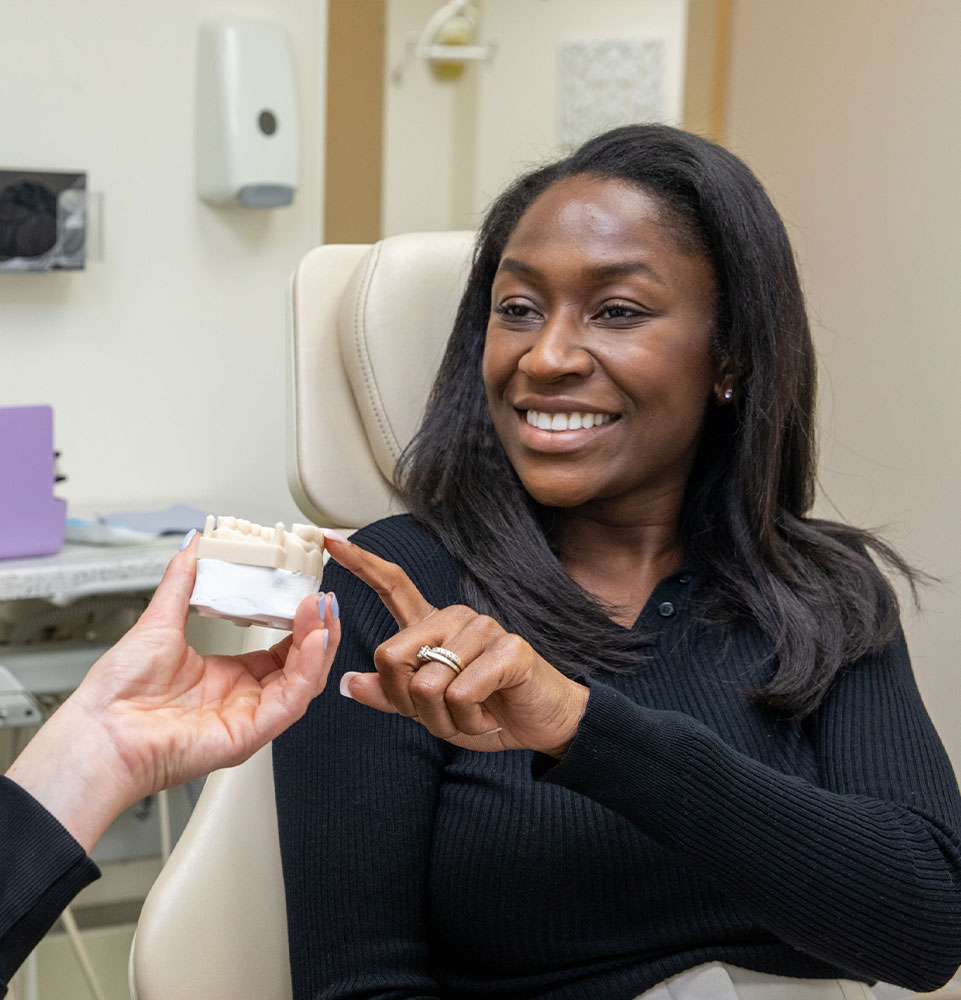 dental implant patient smiling pointing at model of implants